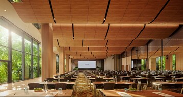 A spacious conference room with long tables, a large screen at the front, and large windows offering a view of greenery.