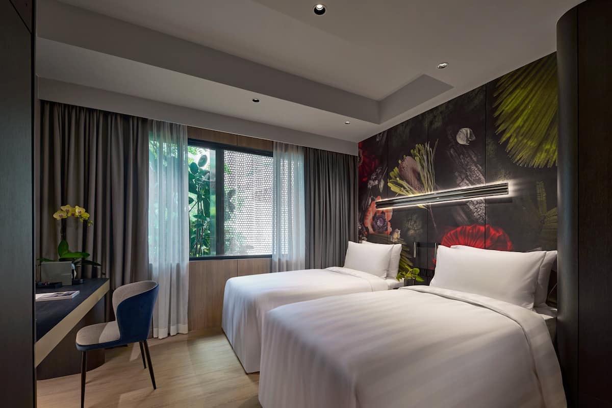 Une chambre d’hôtel moderne avec deux lits, un bureau et une grande fenêtre avec des rideaux.