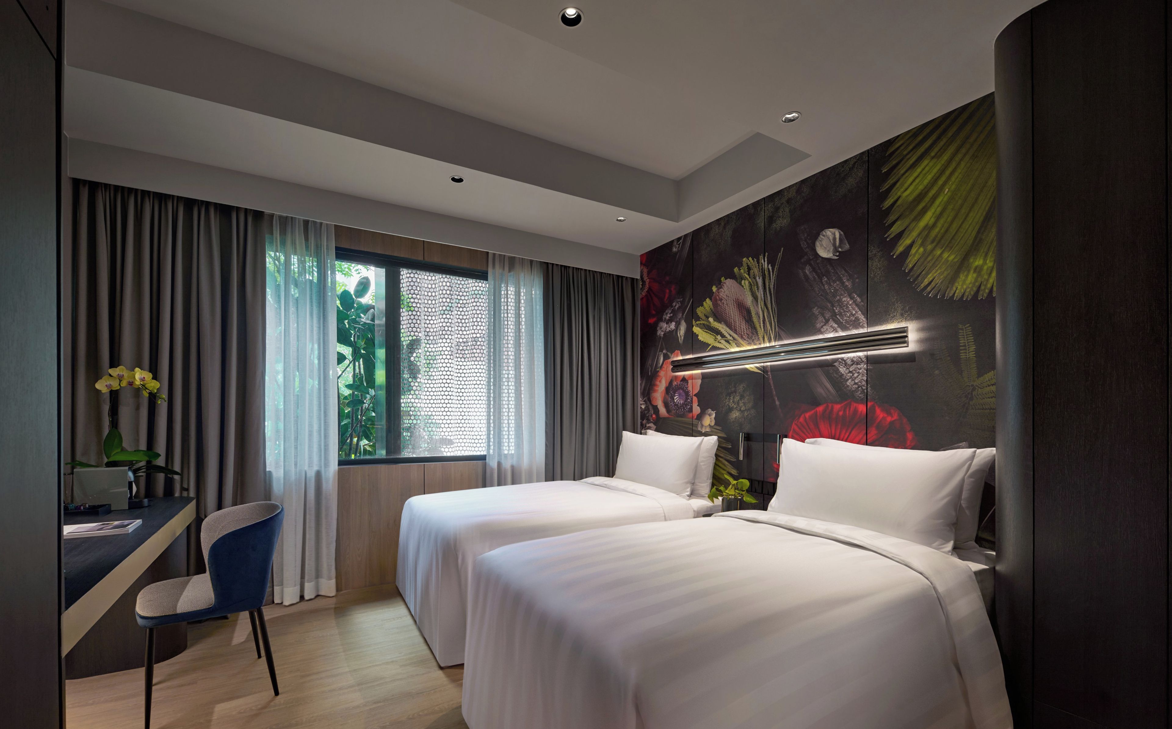 Ein Hotelzimmer mit zwei Betten, einem Schreibtisch, einem Stuhl und einem großen Fenster mit Vorhängen.