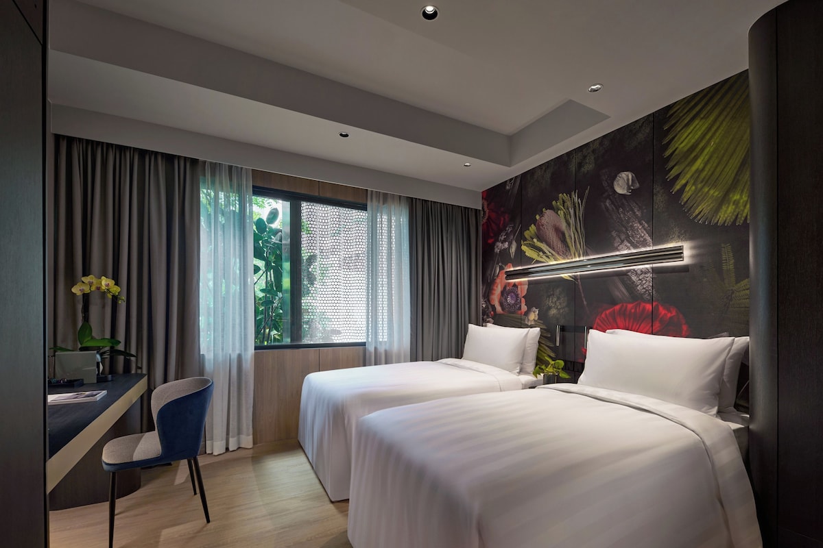 A modern hotel room with two beds, a desk, and a large window with curtains.