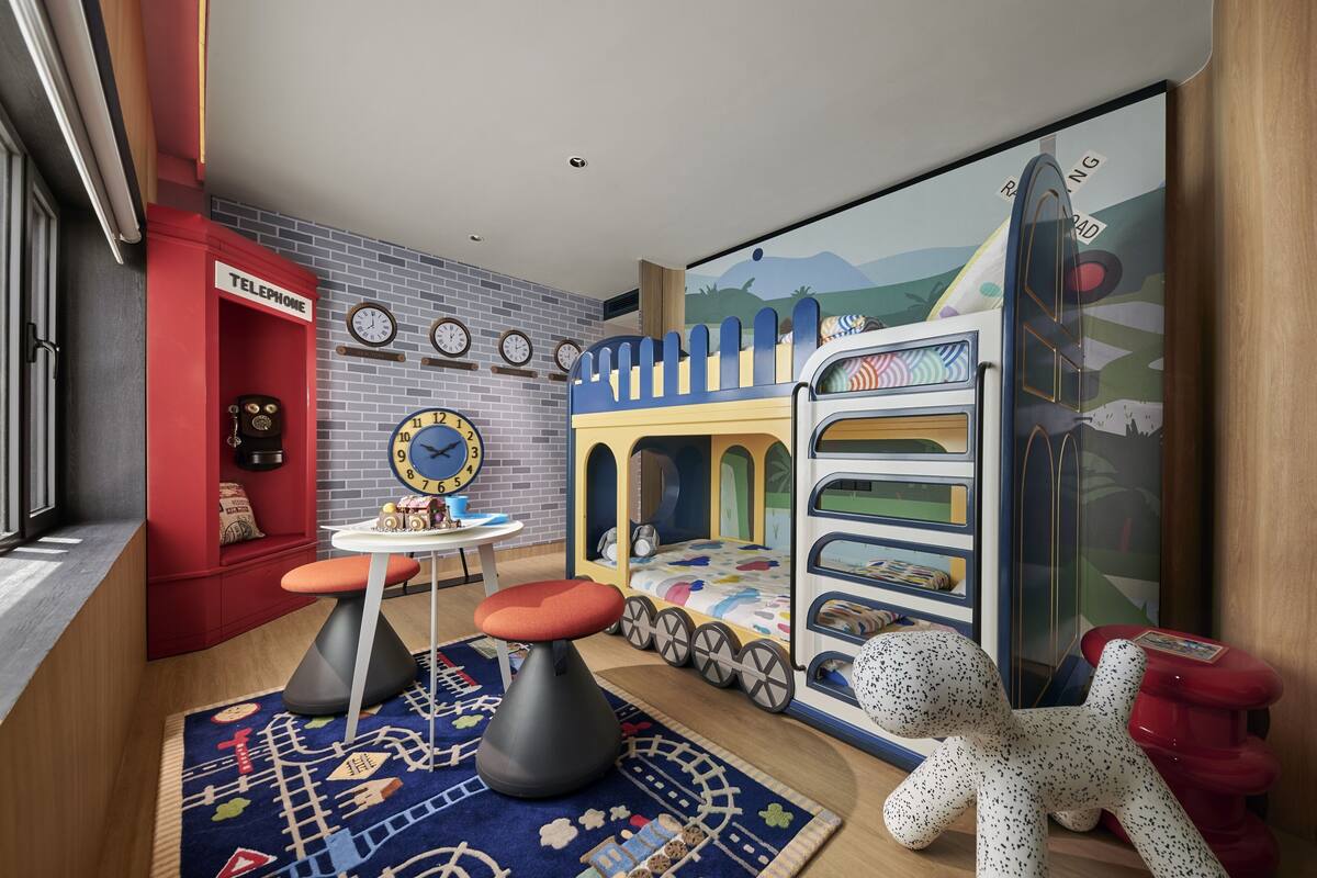 Une salle de jeux pour enfants avec un lit superposé, une petite table avec une horloge et un téléphone public rouge.