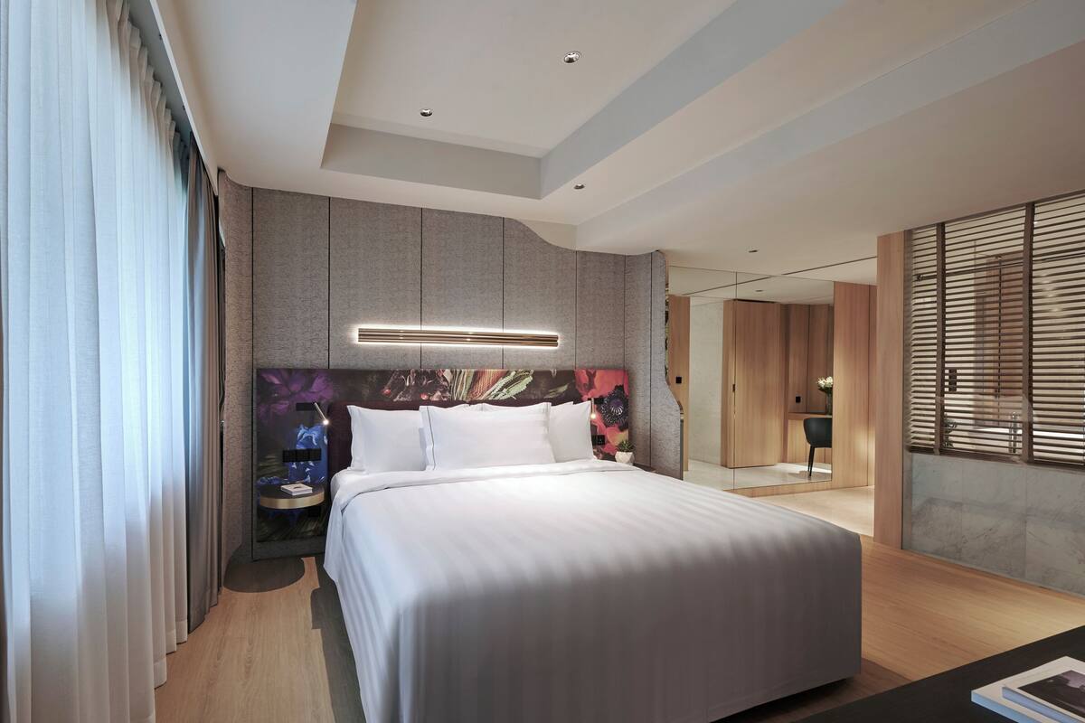 Une chambre d’hôtel moderne avec un grand lit, une table de chevet, un miroir et une vue sur la ville.