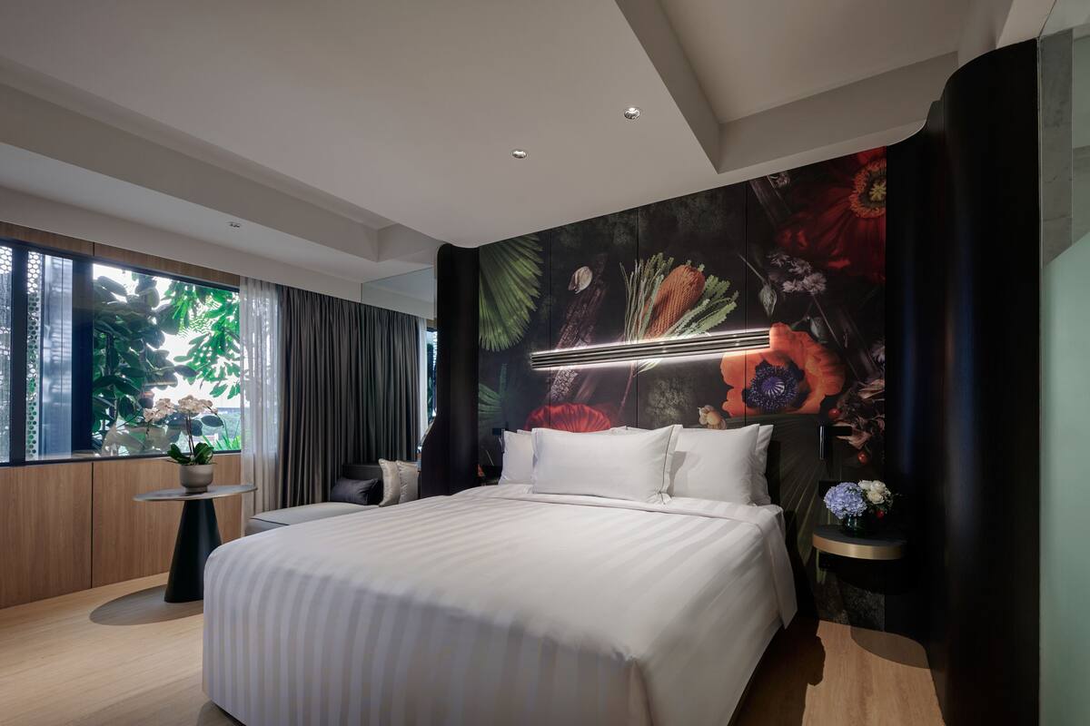Une chambre moderne avec un grand lit, une vue sur la verdure par la fenêtre et une fresque florale sur le mur.