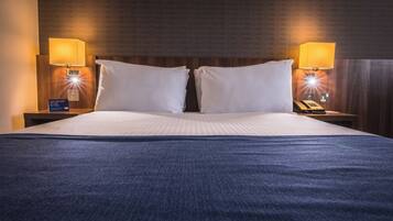 Una habitación de hotel con una cama grande, dos lámparas de noche y una mesita de noche con un teléfono y un reloj digital.