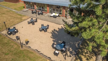 An outdoor patio area with multiple tables and chairs, surrounded by gravel and a wooden fence.