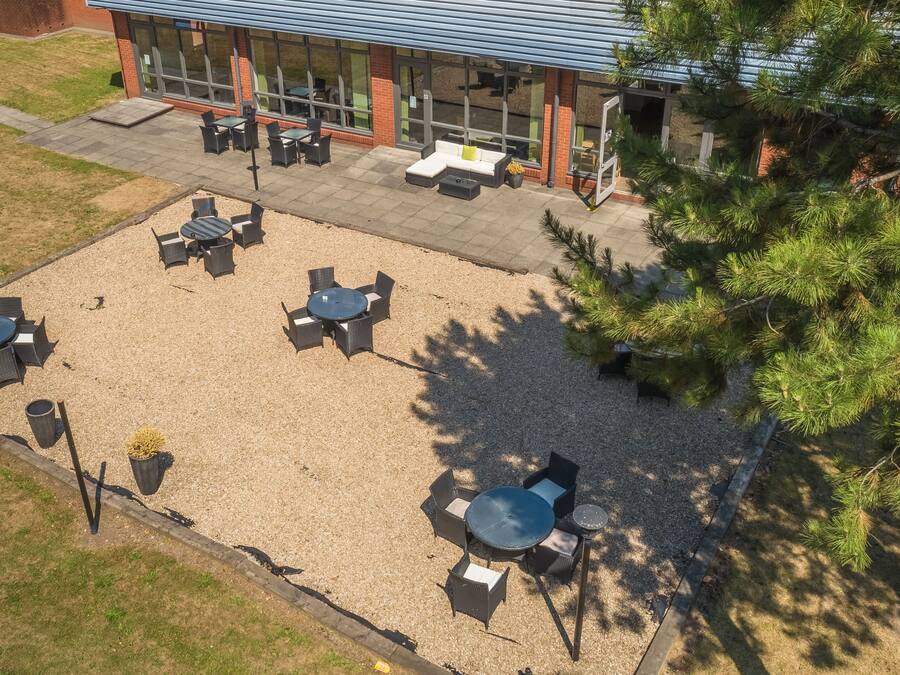 An outdoor patio area with multiple tables and chairs, surrounded by gravel and a wooden fence.