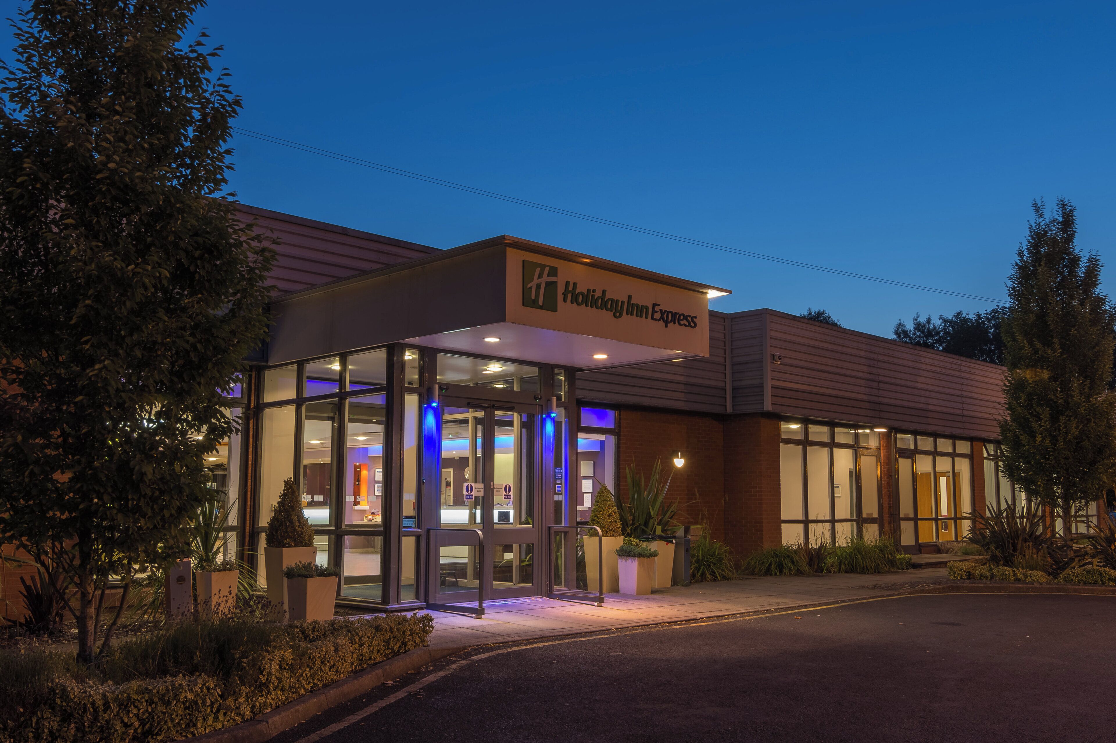 A Holiday Inn Express hotel with a glass entrance, outdoor seating, and a well-lit facade.