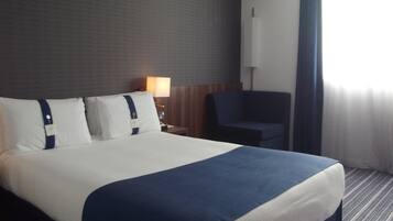 Una camera d'albergo con un letto grande, un comodino con una lampada, una sedia e una finestra con tende.