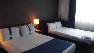 A hotel room with two beds, a nightstand with a lamp, and a window with curtains.
