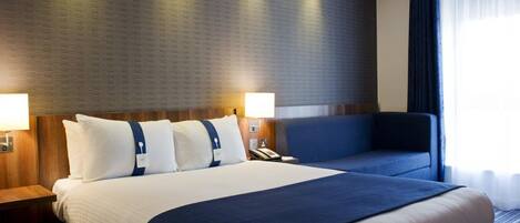 Una habitación de hotel con una cama grande, dos mesitas de noche, un escritorio y una silla.