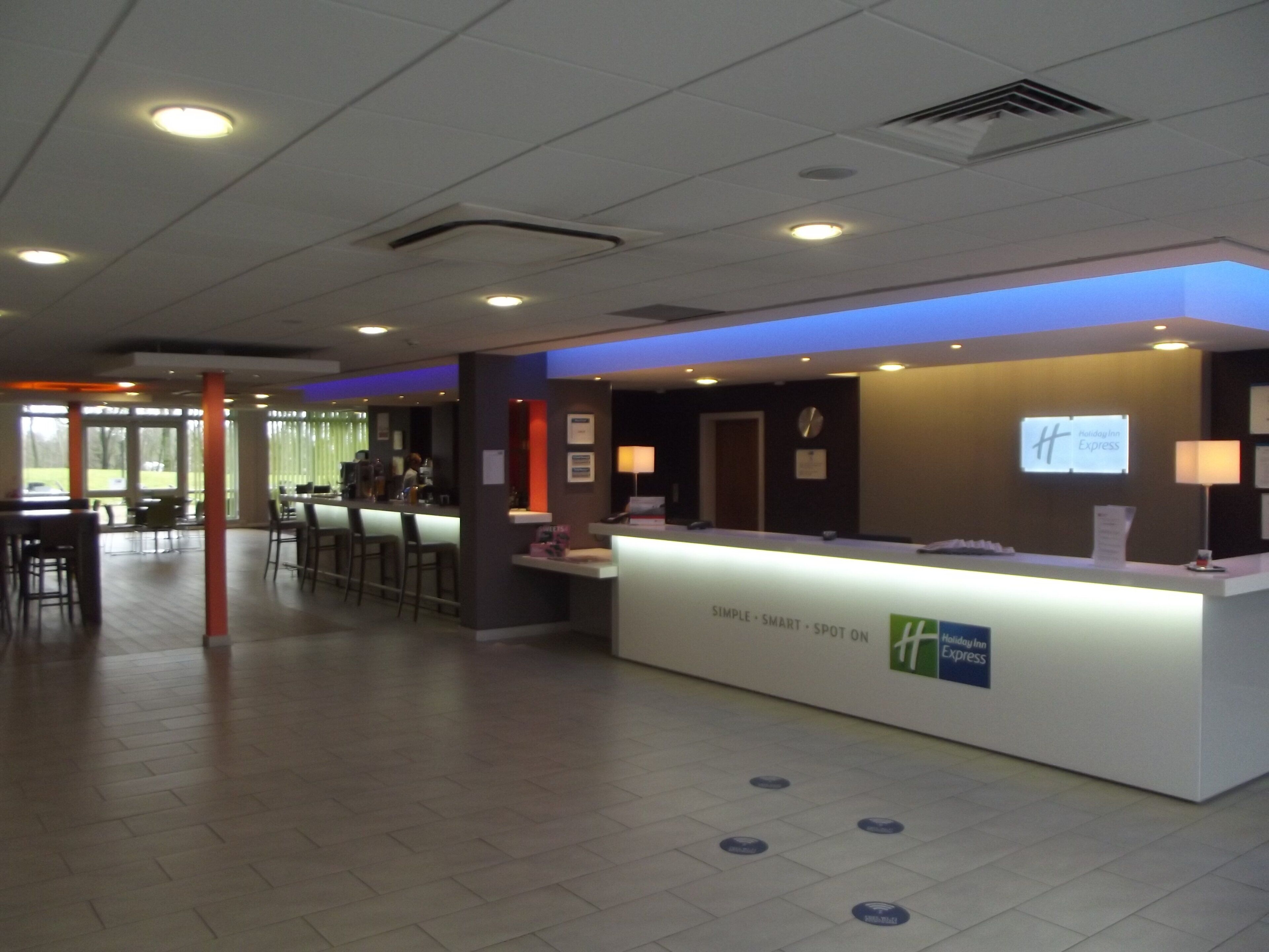 Ein Hotelrezeptionstresen mit digitaler Anzeige, einer Uhr und einem Schild für Holiday Inn Express.