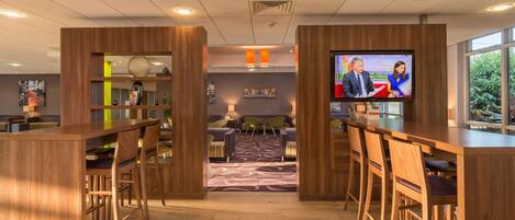 A modern bar area with wooden furniture and a television screen displaying a news program.