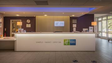 Mostrador de recepción de Holiday Inn Express con un diseño moderno, que incluye un reloj y una pantalla digital que muestra el nombre del hotel.