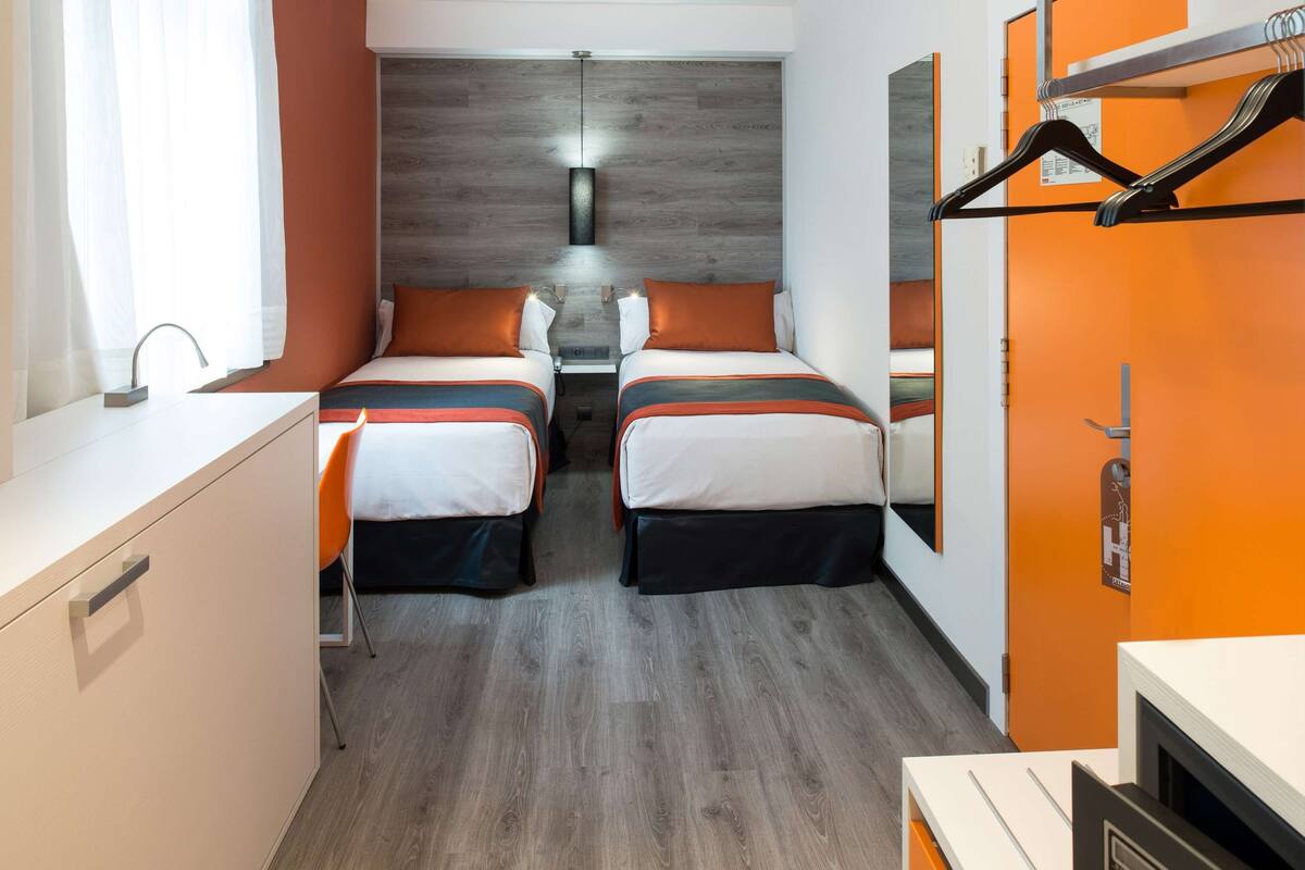 A hotel room with two beds, a desk, and a mirror.