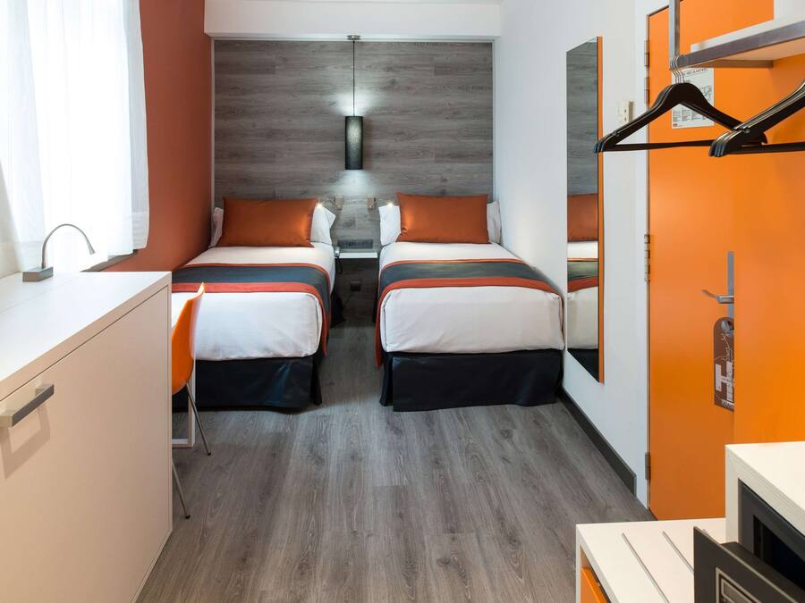 Una habitación de hotel con dos camas, un escritorio y un espejo.