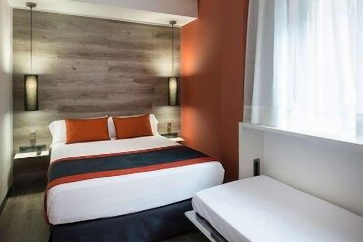 A hotel room with a bed, bedside tables, a window with curtains, and a wooden wall.