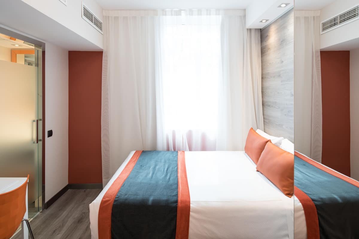 A hotel room with a large bed, a desk, and a window with curtains.