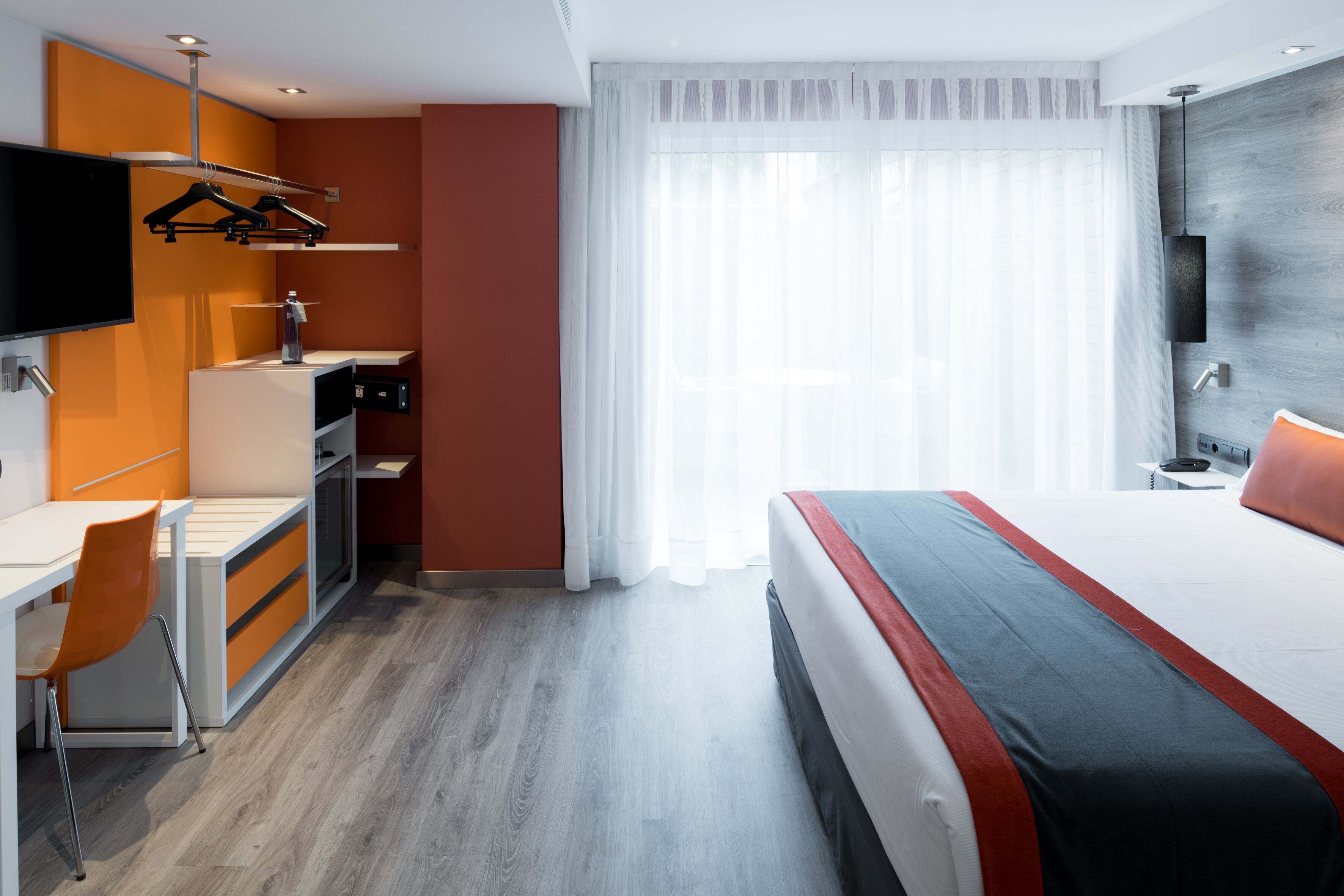 Une chambre d’hôtel moderne équipée d’un lit, d’un bureau, d’une chaise et d’un téléviseur fixé au mur.