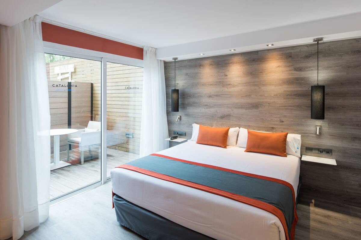A modern hotel room with a large bed, a sliding glass door to a balcony, and a wooden accent wall.