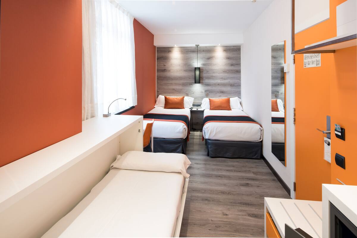 A hotel room with two beds, a large window, a mirror, and a wooden accent wall.