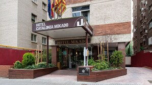 The entrance of Hotel Catalonia Mikado with a modern facade, a covered entrance, and flags. - Catalonia Mikado (Barcelona)