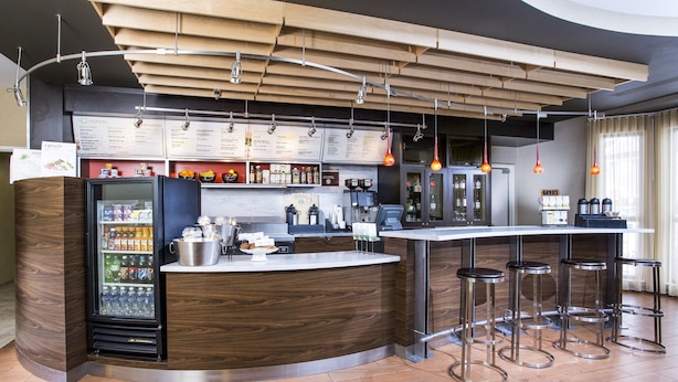 A modern bar area with a wooden counter, bar stools, a refrigerator stocked with beverages, and hanging pendant lights.