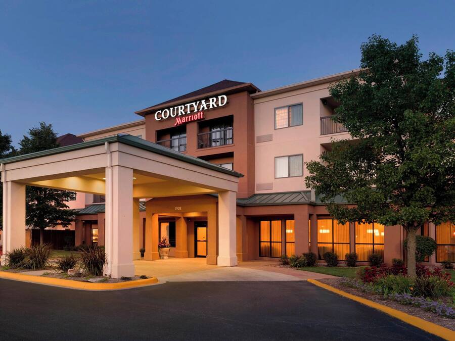 Um hotel Courtyard Marriott com entrada coberta, vários andares e um jardim ajardinado.