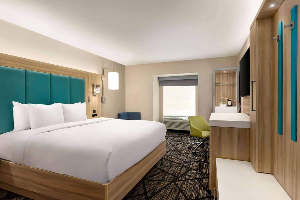 A hotel room with a large bed, a desk with a chair, a window, and a mirror.
