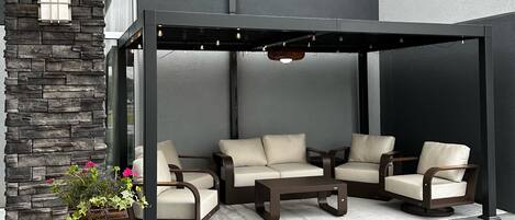 Uma área de estar ao ar livre com parede de pedra, pérgola e planta em vaso.