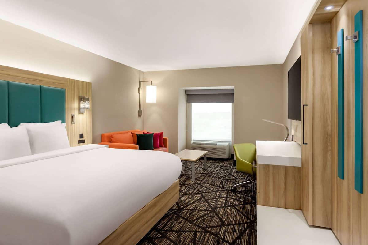 A hotel room with a large bed, a desk, a chair, a window, and a bathroom area.