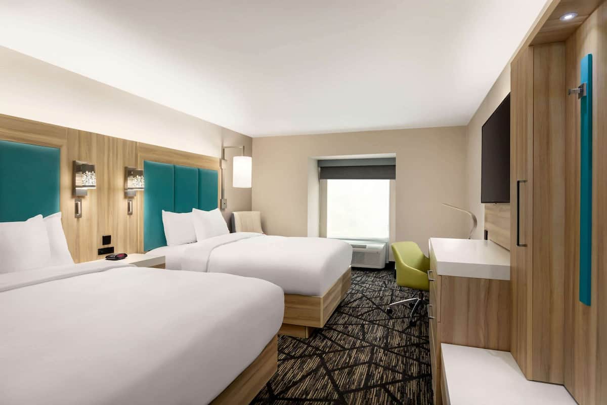 A hotel room with two beds, a desk, a chair, and a TV.