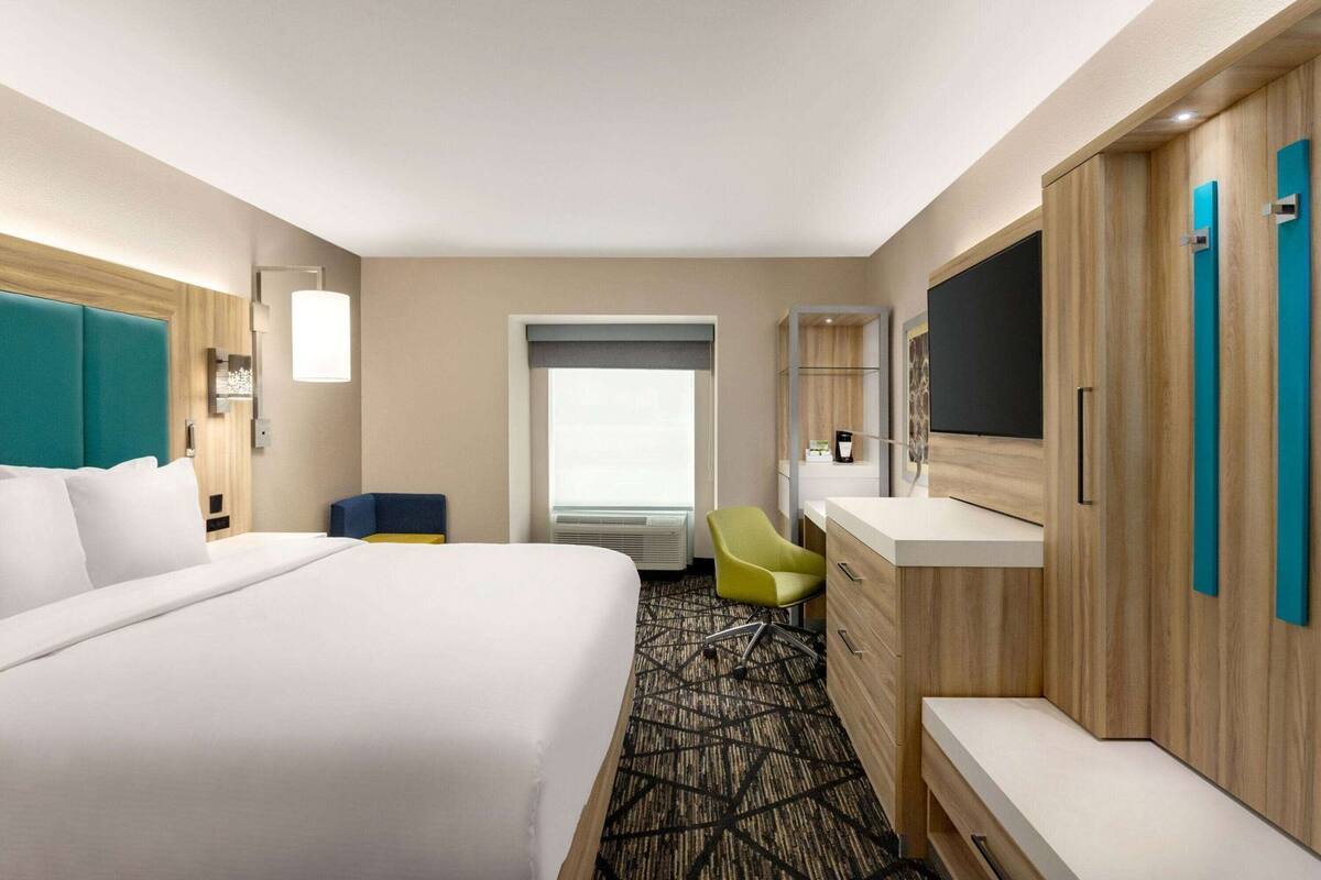A hotel room with a large bed, a desk, a chair, a TV, and a wardrobe.