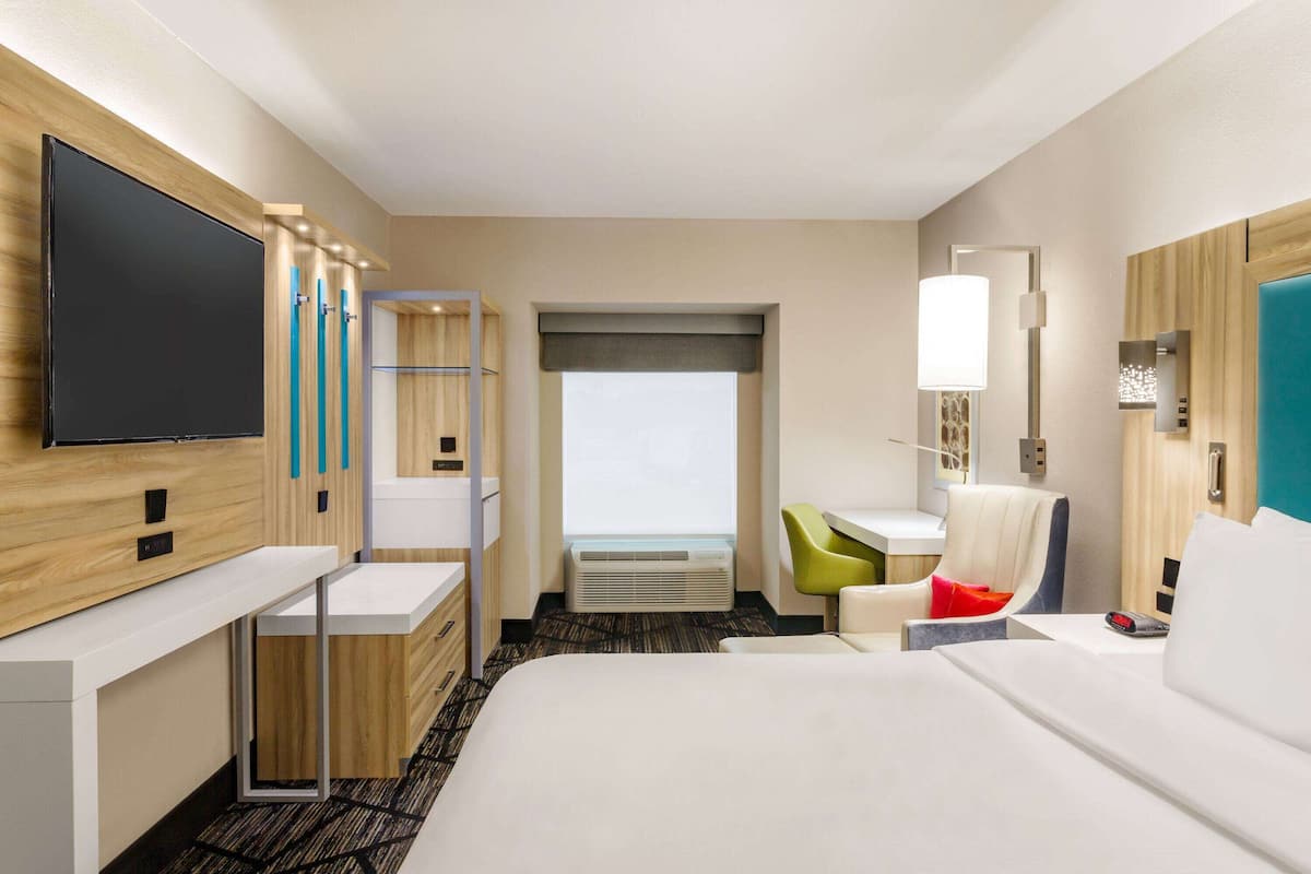 A hotel room with a bed, a desk, a chair, a TV, and a window.