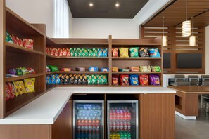 Un mostrador de aperitivos con estantes llenos de diferentes papas fritas y una vitrina refrigerada con bebidas.