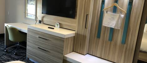 A hotel room with a desk, a chair, a TV, a wardrobe, and a bed.