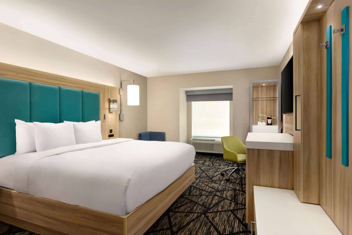A hotel room with a large bed, a desk, a chair, a window, and a bathroom area.