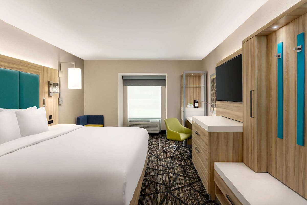 A hotel room with a large bed, a desk, a chair, a TV, and a window.