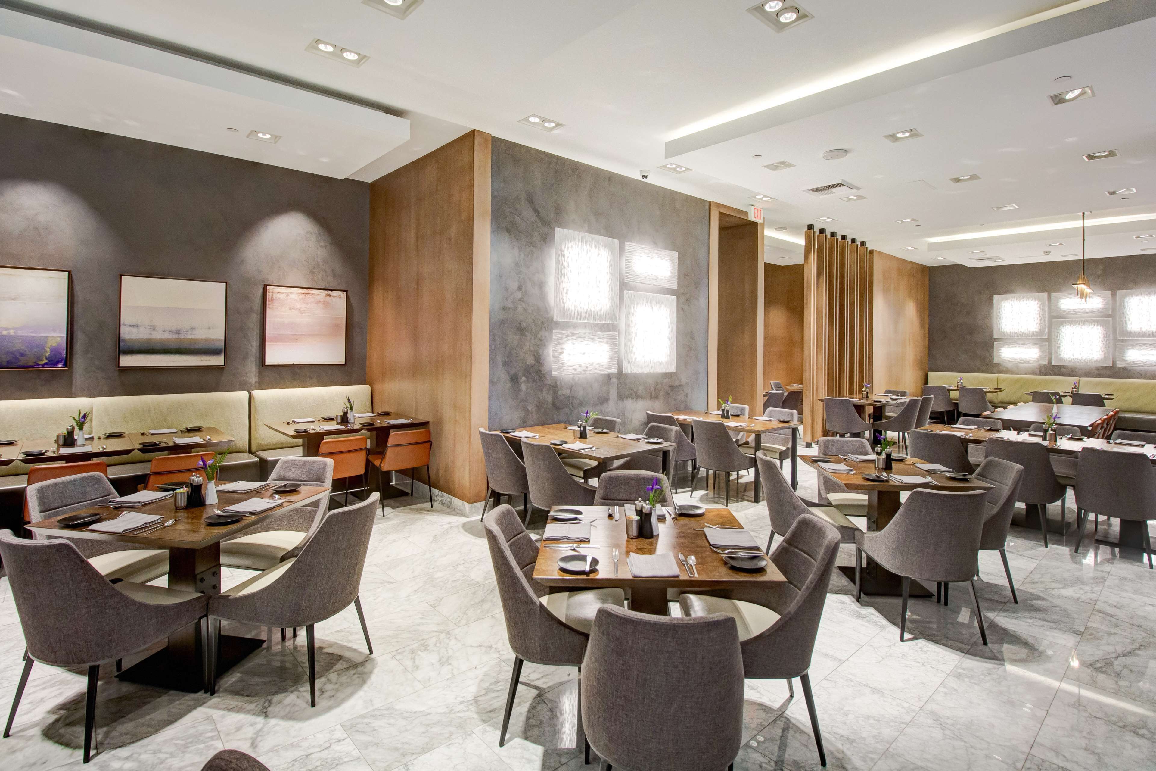 Een modern restaurant met meerdere eettafels en stoelen, een bar en kunstwerken aan de wanden.