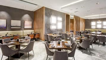 Een modern restaurant met meerdere eettafels en stoelen, een bar en kunstwerken aan de wanden.