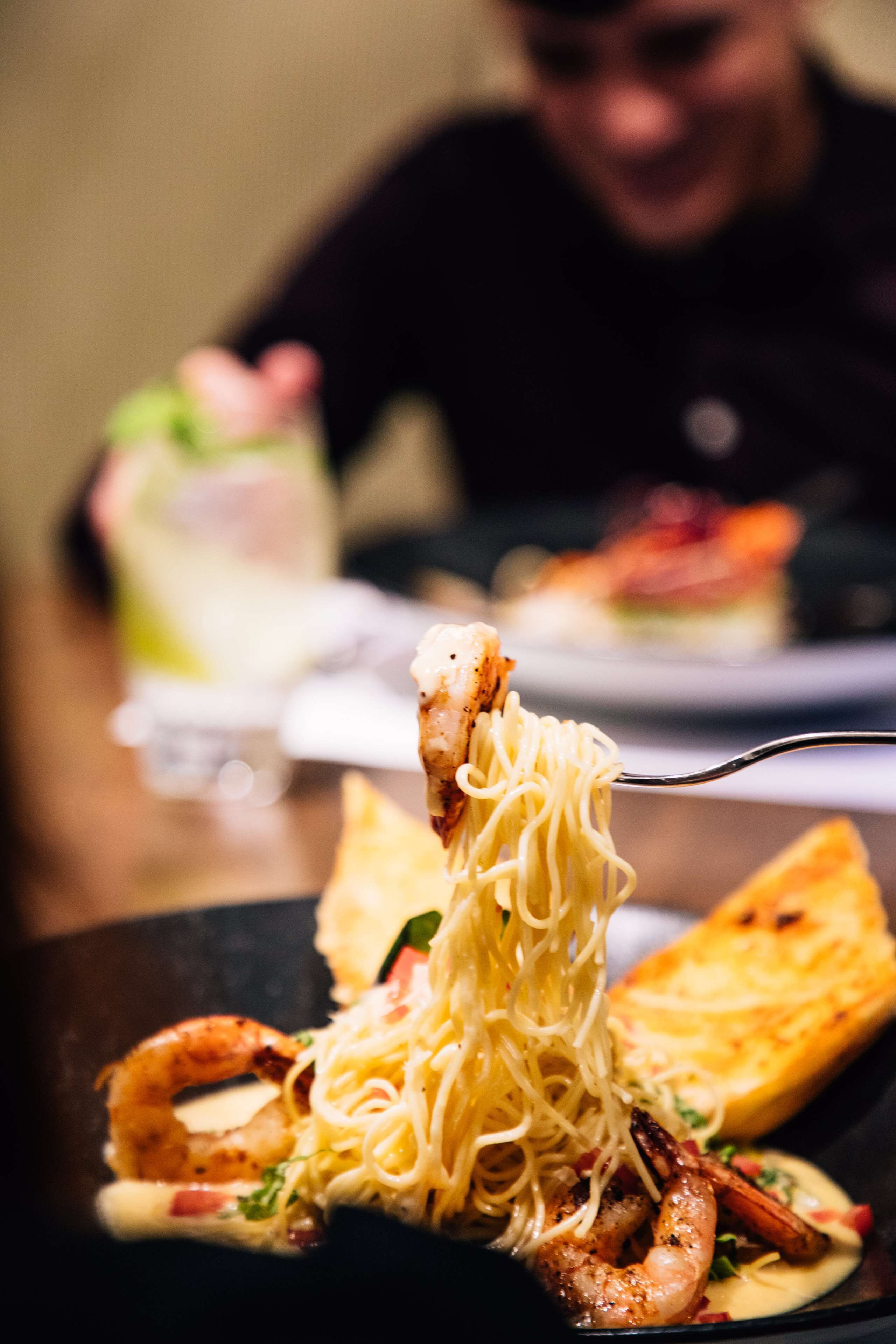 A plate of spaghetti with shrimp and a slice of bread.