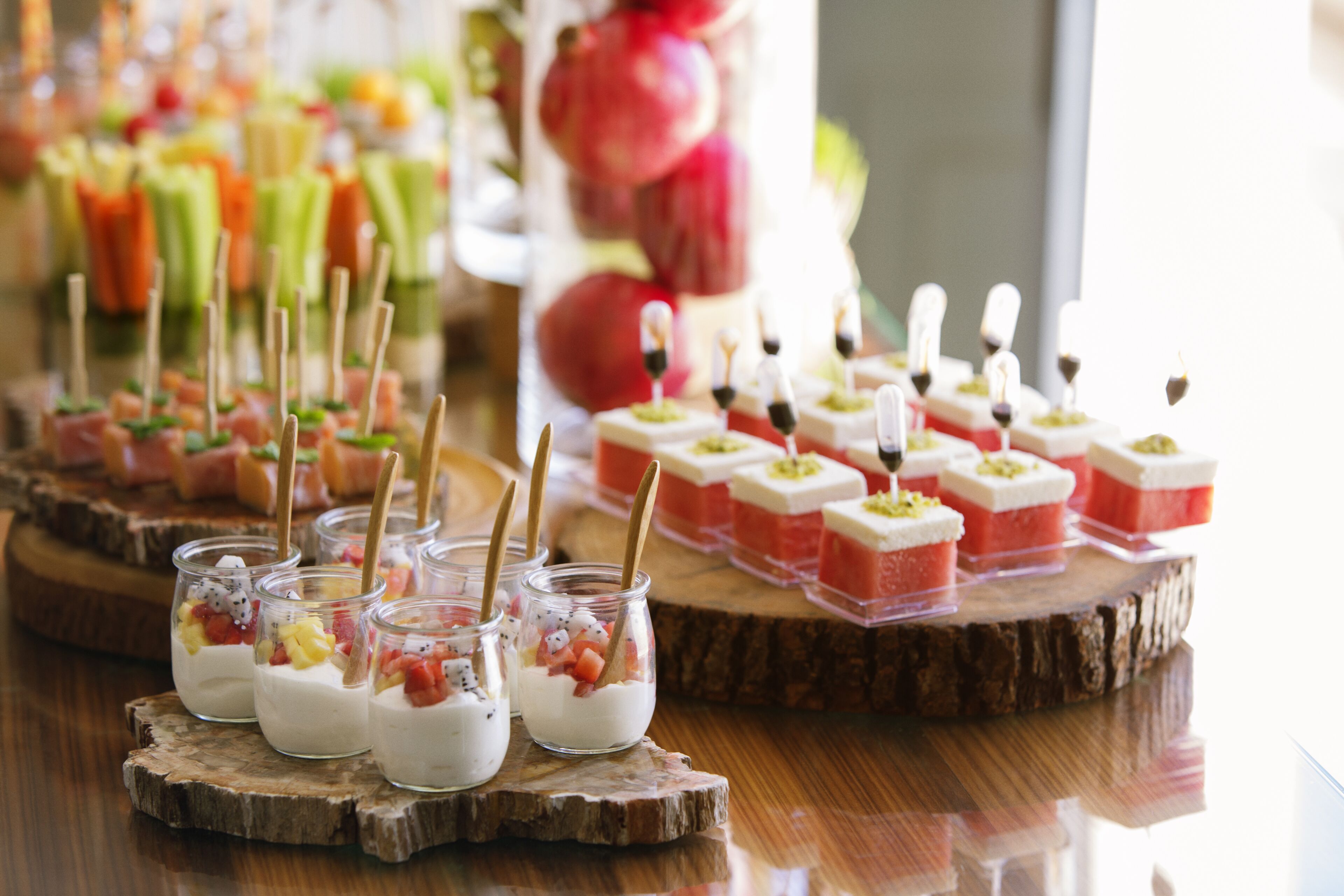 A variety of desserts on wooden serving boards, including fruit-topped yogurt cups and small square desserts with a red base.