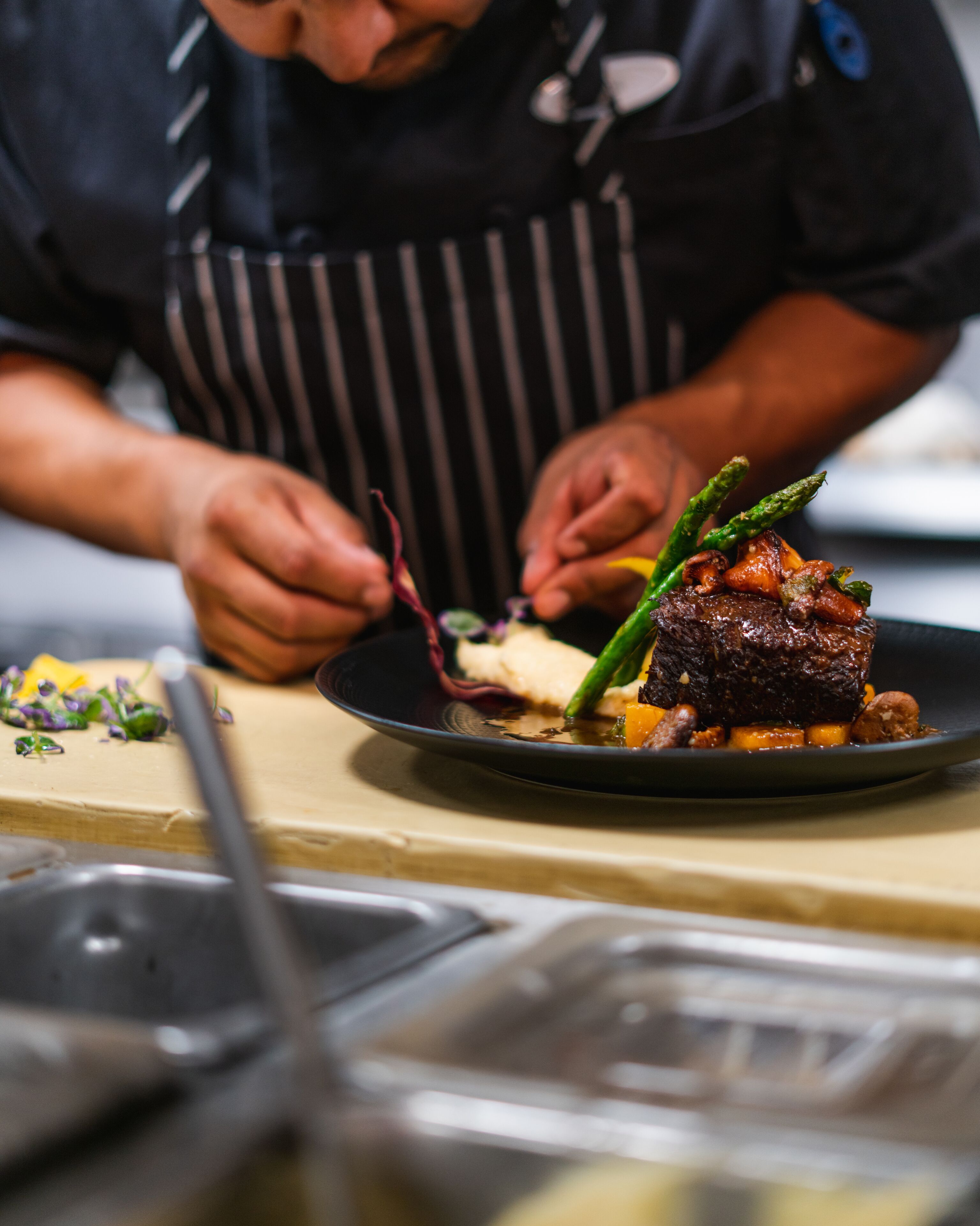 A chef preparing a dish with a steak and vegetables on a plate.