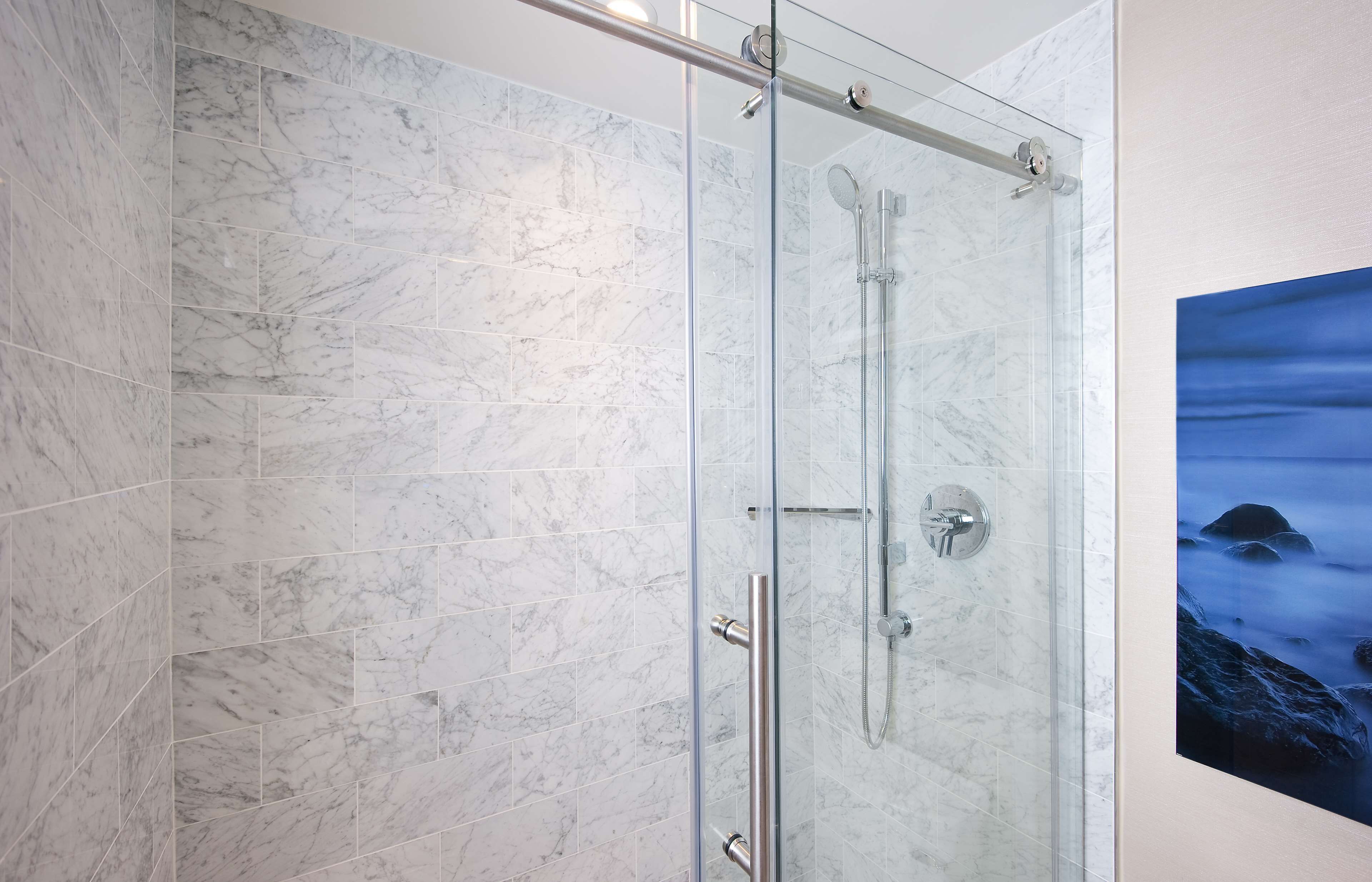 A glass-enclosed shower with a marble tile wall, a glass door, and a showerhead.