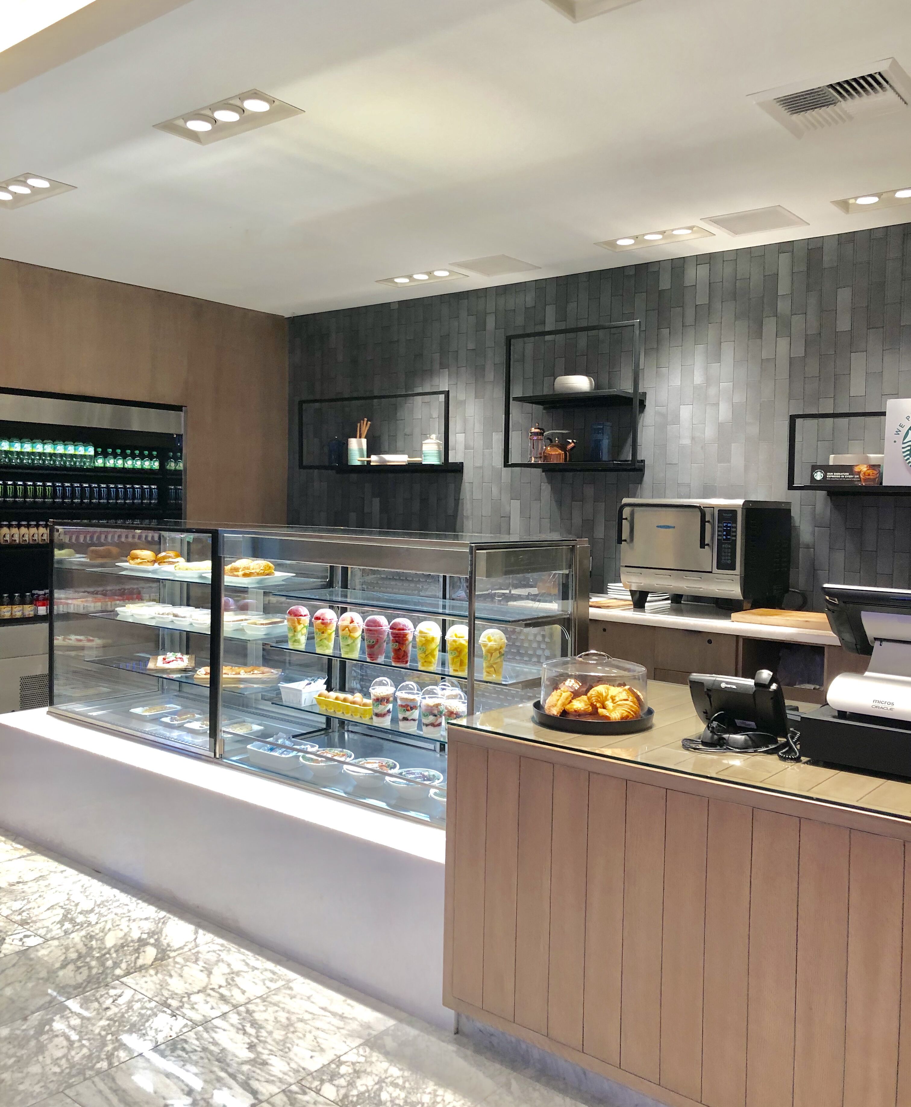 A modern cafe with a glass display case filled with colorful beverages and pastries, a coffee machine, and a microwave on the counter.