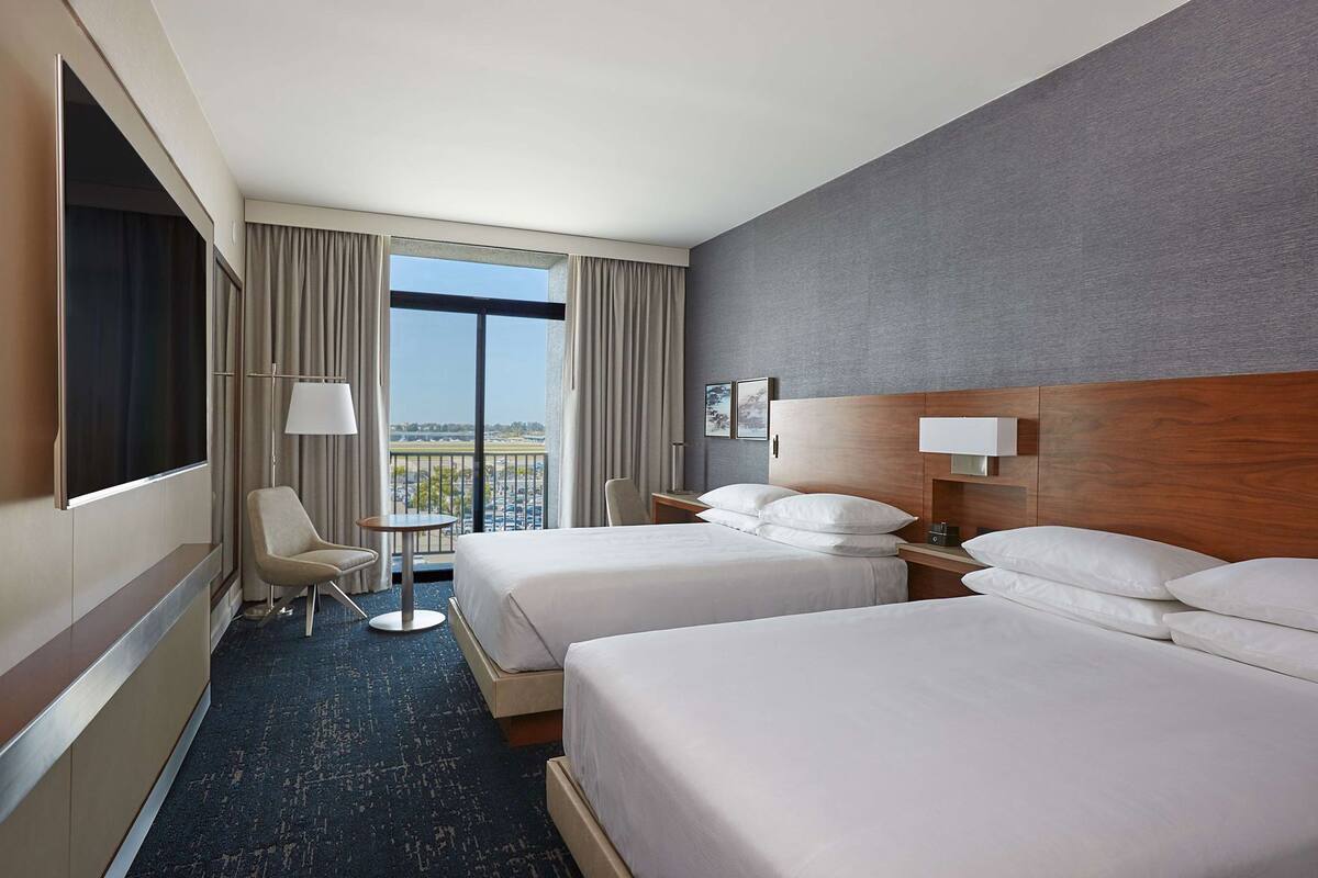 Ein Hotelzimmer mit zwei Betten, einem Schreibtisch, einem Stuhl, einem Fernseher und Blick auf die Stadt.