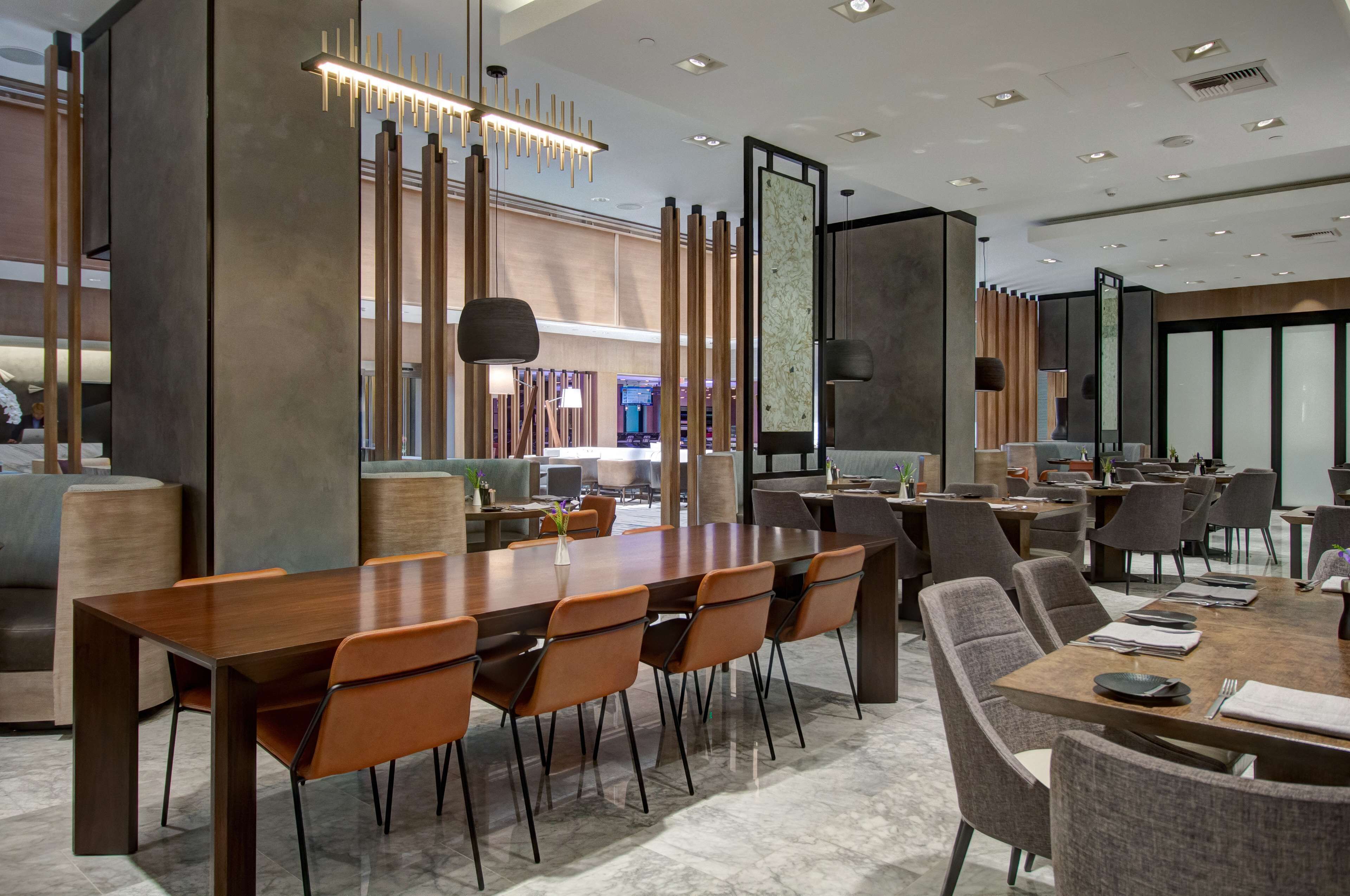 A modern conference room with a long wooden table, multiple chairs, and contemporary lighting fixtures.