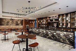 Una zona de bar moderna con mostrador de mármol, taburetes y una variedad de botellas y vasos.