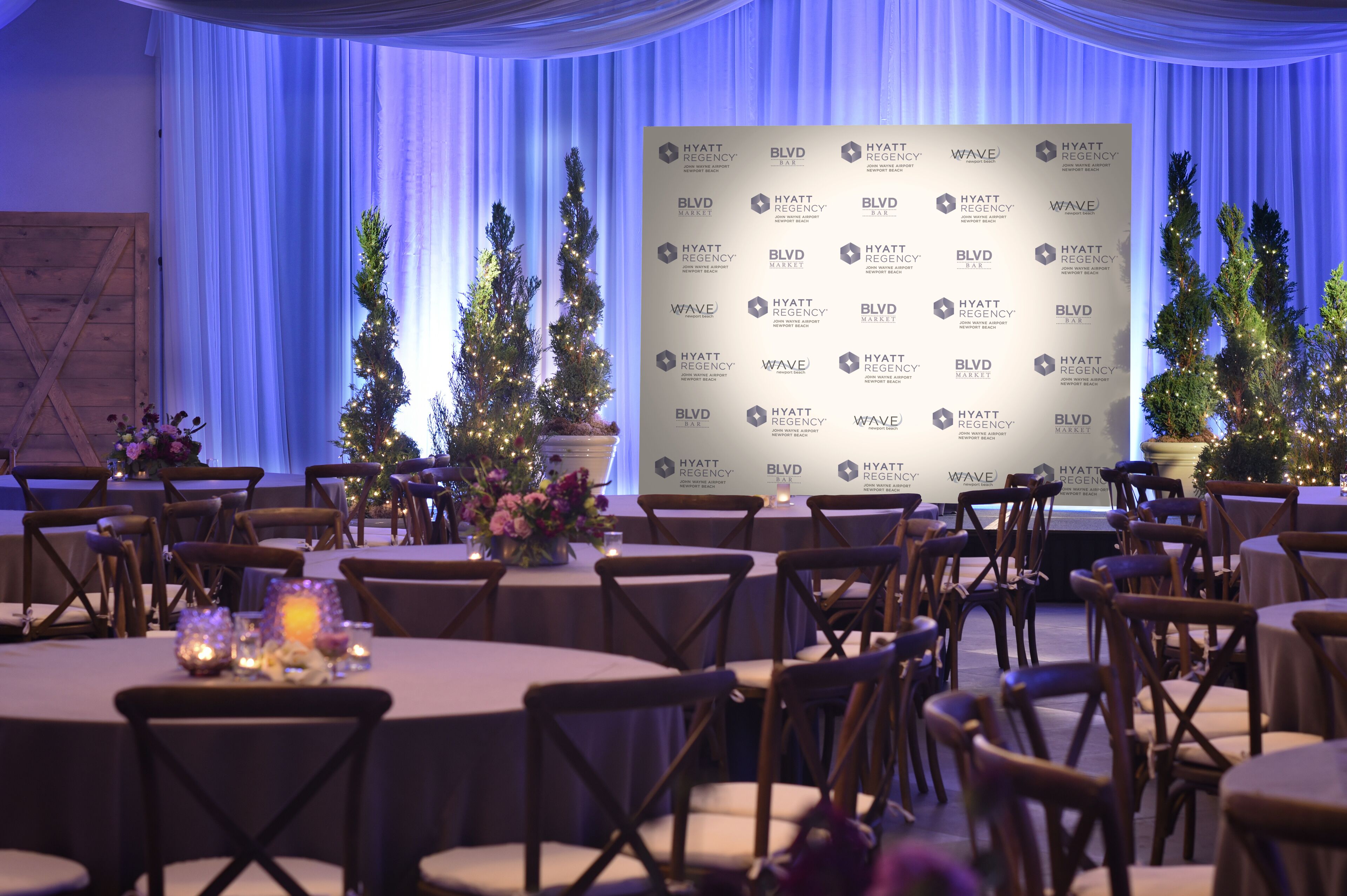 Une salle de banquet avec des tables rondes, des chaises en bois et des sapins de Noël.