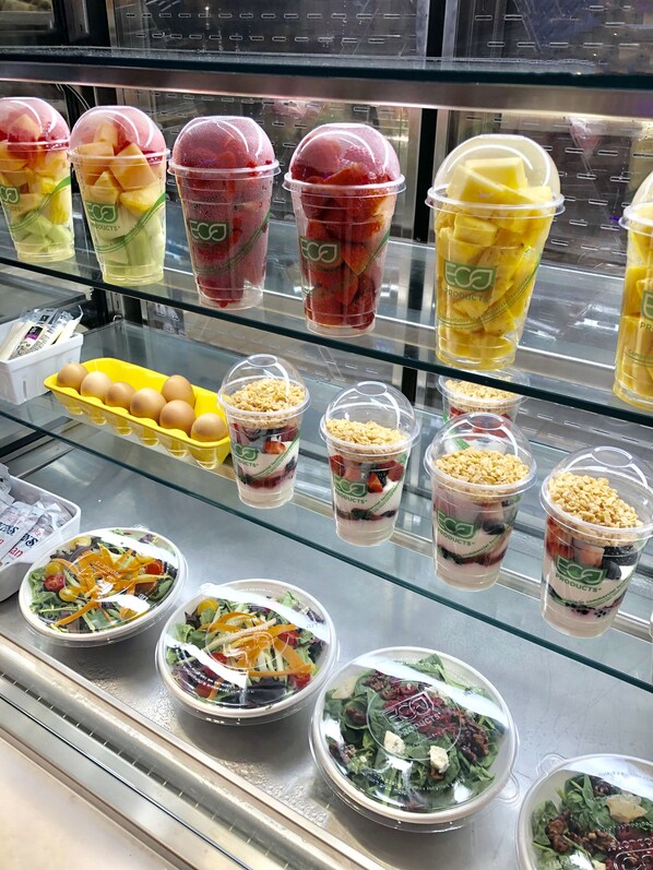A variety of food items displayed in a refrigerated case, including fruit cups and salad bowls.