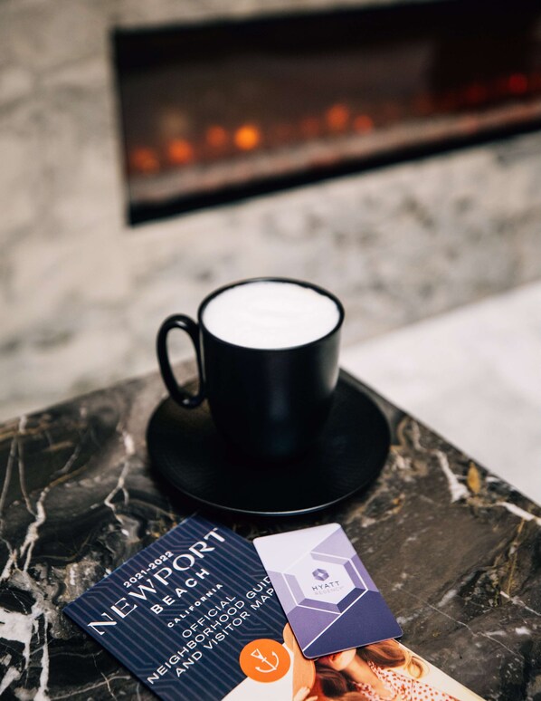 A black coffee cup on a marble table with a brochure and a card beside it.